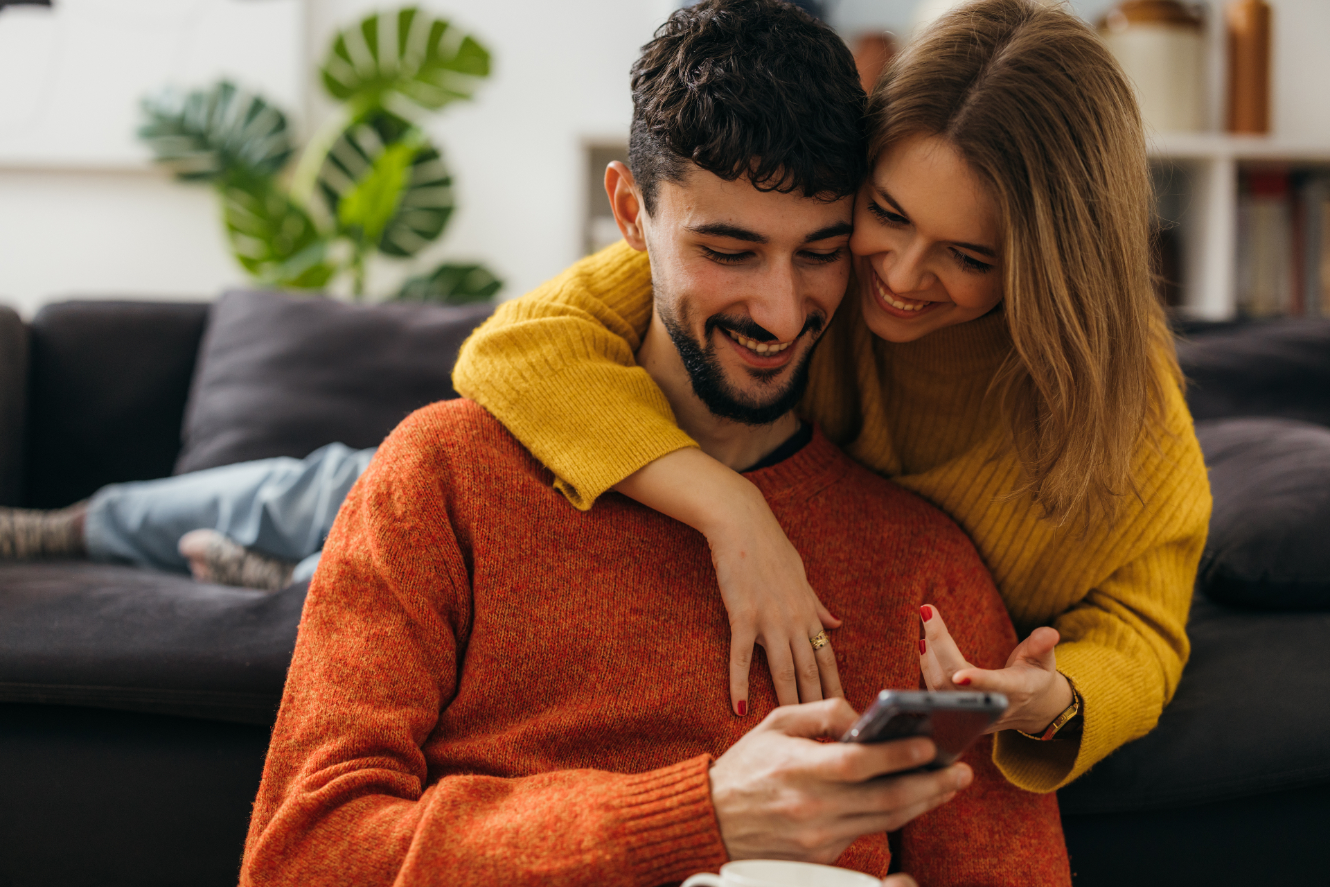 Casal sorridente consultando o aplicativo Hapvida no sofá de casa